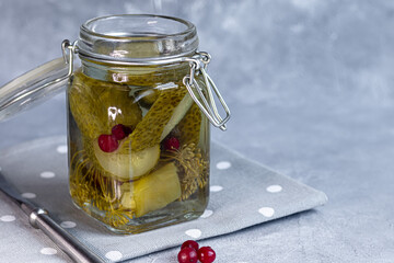Pickled cucumbers in a glass jar and on a wooden board. Fermented food on a gray background.