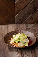 Caesar salad with grilled chicken, tomato, boiled egg, lettuce, croutons and green sauce. Close-up on a brown round plate, isolated on a wooden background with copy space. Healthy food menu.