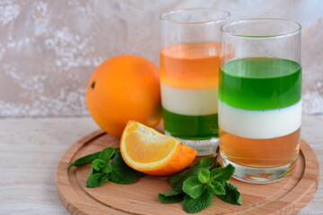 two glasses with kiwi milk and orange jelly on the wooden cutting board