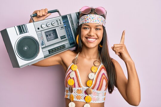 Beautiful hispanic woman wearing hippie style holding boom box smiling with an idea or question pointing finger with happy face, number one