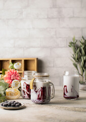 Bilberry or blueberry milkshake in glass bottle with fresh berries in ceramic plate and beautiful flowers on background.Healthy cocktail with vegan milk.