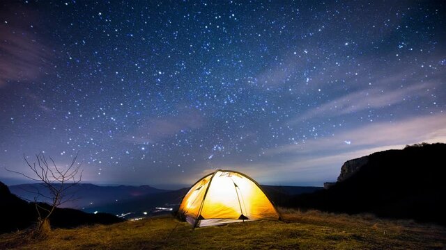 Glowing camping tent in the mountains under the twinkling starry sky. Cinemagraph.