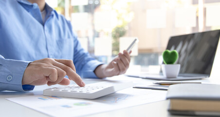 Asian male employees are analyzing market data via smartphones and have laptops to calculate the company's finances In a private office at home, Working at home and new normal concept.