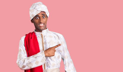 African handsome man wearing tradition sherwani saree clothes pointing aside worried and nervous...