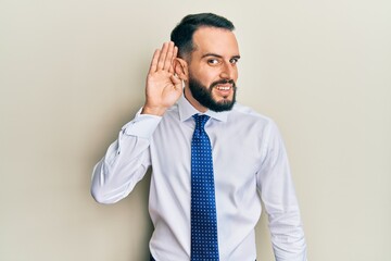 Young man with beard wearing business tie smiling with hand over ear listening an hearing to rumor or gossip. deafness concept.