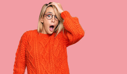 Beautiful blonde woman wearing casual clothes and glasses surprised with hand on head for mistake,...