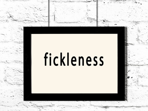 Black frame hanging on white brick wall with inscription fickleness