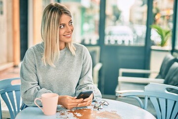 Young blonde girl smiling happy using smartphone at coffee shop.