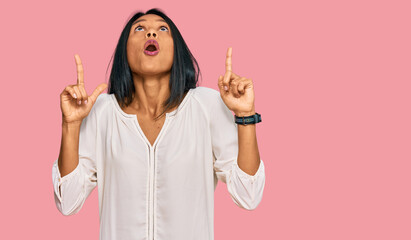 Young african american woman wearing casual clothes amazed and surprised looking up and pointing with fingers and raised arms.