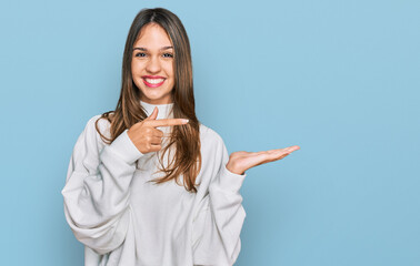 Young brunette woman wearing casual turtleneck sweater amazed and smiling to the camera while presenting with hand and pointing with finger.