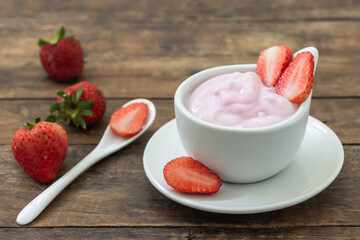 Yogurt strawberry in white cup on plate and wooden floor with fresh strawberry on top, food for healthy.