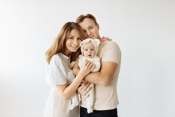 Portrait of a happy young family, with a little adorable daughter. Caring parents hold and gently hug their baby. Together they pose for a photo, looking at the camera. Family concept.