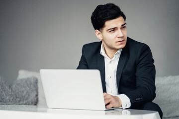 communicates on a social network on a laptop. my favorite job is senior economist at a bank. a dark-haired man of European appearance in a black business suit. sitting in a modern office.