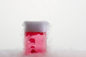 Glass jar with red chemical and smoke.  Sublimation of dry ice on a white background. Beaker on the lab table.