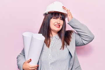 Young plus size woman holding paper blueprints stressed and frustrated with hand on head, surprised...