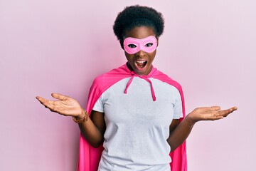 Young african american girl wearing superhero mask and cape costume celebrating crazy and amazed...