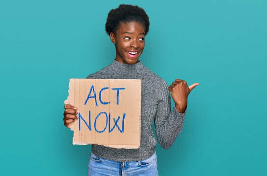 Young african american girl holding act now banner pointing thumb up to the side smiling happy with open mouth