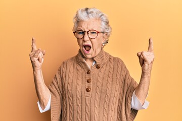 Senior grey-haired woman wearing casual clothes and glasses shouting with crazy expression doing...