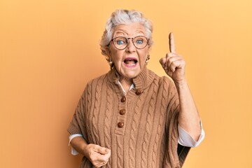 Senior grey-haired woman wearing casual clothes and glasses pointing finger up with successful idea. exited and happy. number one.