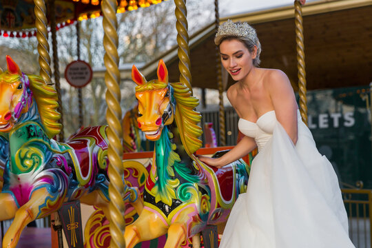 the bride in a white wedding dress walks next to the carousel horse,
