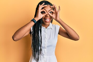 African american woman wearing casual clothes doing ok gesture like binoculars sticking tongue out, eyes looking through fingers. crazy expression.