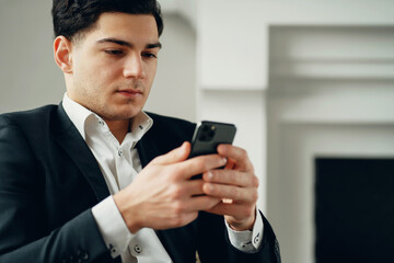 chat in a social network chat with friends and partners. The manager is a man in a business suit sitting in a modern office. prints a text message in the phone. a convenient application.