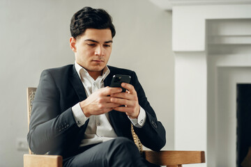 a convenient application. chat in a social network chat with friends and partners. The manager is a man in a business suit sitting in a modern office. prints a text message in the phone.