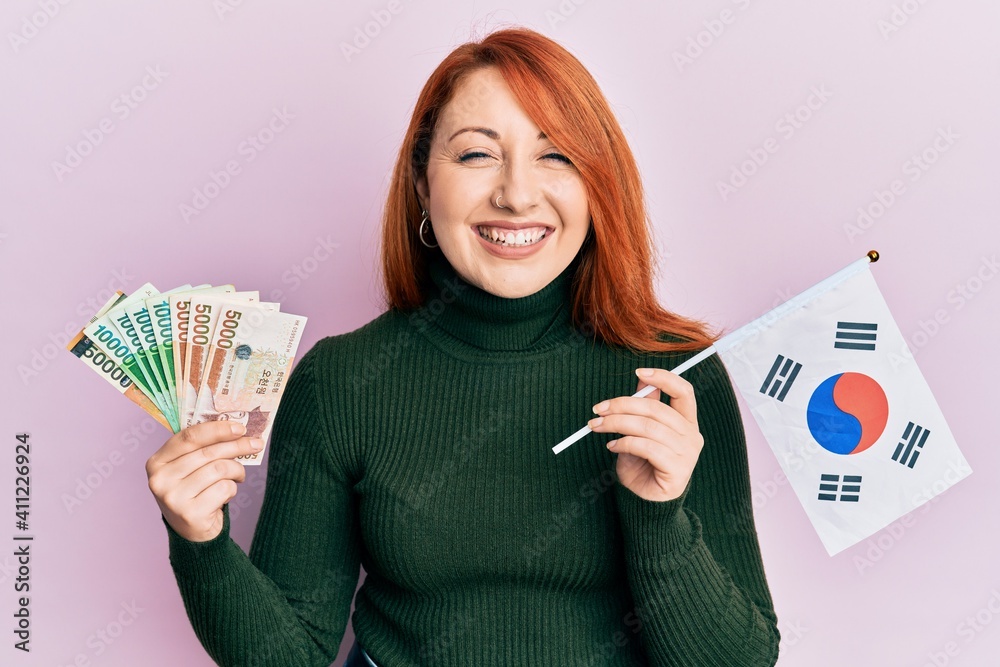 Poster beautiful redhead woman holding south korean won banknotes and flag smiling and laughing hard out lo