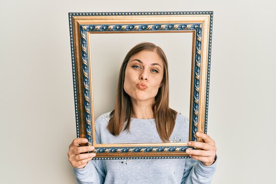 Beautiful caucasian woman holding empty frame looking at the camera blowing a kiss being lovely and sexy. love expression.