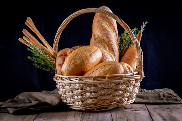 Variety of breads in basket on wooden table in dark background. Bakery Assortment.