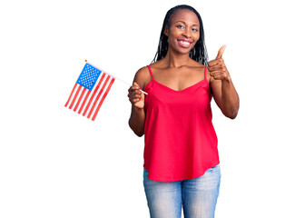 Young african american woman holding united states flag smiling happy and positive, thumb up doing excellent and approval sign