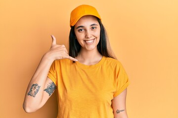 Young hispanic woman wearing delivery uniform and cap smiling doing phone gesture with hand and fingers like talking on the telephone. communicating concepts.
