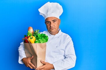 Mature middle east man professional chef holding bag of groceries thinking attitude and sober expression looking self confident