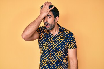 Handsome hispanic man with beard wearing 80s disco style shirt surprised with hand on head for mistake, remember error. forgot, bad memory concept.