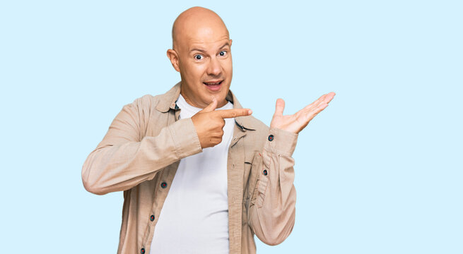 Middle age bald man wearing casual clothes amazed and smiling to the camera while presenting with hand and pointing with finger.
