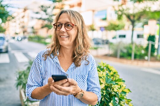 Middle age caucasian woman smiling happy using smartphone at the city.