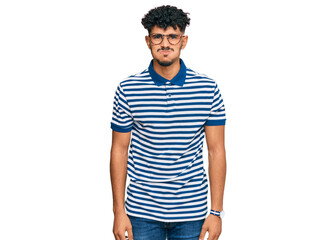 Young arab man wearing casual clothes and glasses puffing cheeks with funny face. mouth inflated...