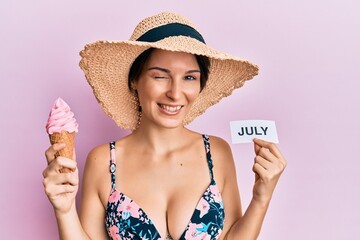 Young brunette woman with short hair holding ice cream and july paper winking looking at the camera...
