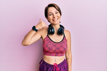 Obraz premium Young brunette woman with short hair wearing sportswear and headphones smiling doing phone gesture with hand and fingers like talking on the telephone. communicating concepts.