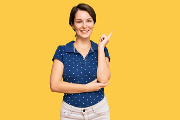 Young brunette woman with short hair wearing casual clothes with a big smile on face, pointing with hand and finger to the side looking at the camera.