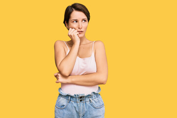 Young brunette woman with short hair wearing casual summer clothes looking stressed and nervous with hands on mouth biting nails. anxiety problem.