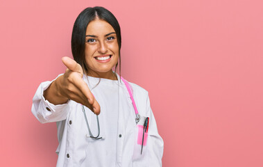 Beautiful hispanic woman wearing doctor uniform and stethoscope smiling friendly offering handshake as greeting and welcoming. successful business.