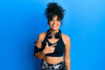 Obraz premium Young hispanic woman wearing gym clothes and using headphones cheerful with a smile of face pointing with hand and finger up to the side with happy and natural expression on face