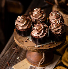 homemade tasty chocolate cupcakes with chocolate cream on wooden cake stand on rustic table. selective focus