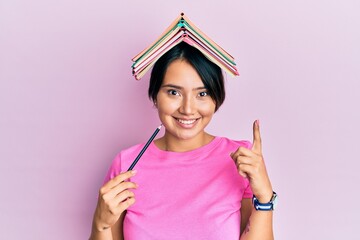 Beautiful young woman with short hair holding book over head smiling with an idea or question pointing finger with happy face, number one