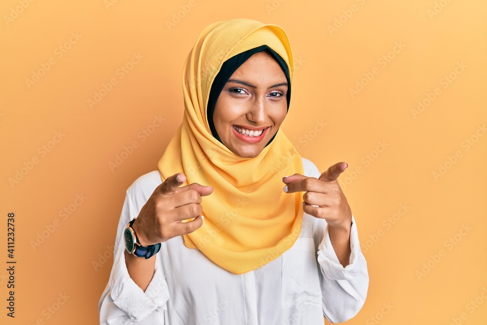 Poster Young brunette arab woman wearing traditional islamic hijab scarf pointing fingers to camera with happy and funny face. good energy and vibes.