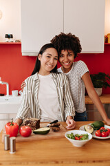 Snapshot of brunette girls looking at camera in kitchen while cutting vegetables