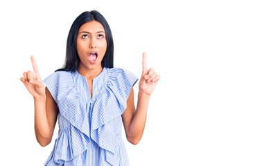 Young beautiful latin girl wearing casual clothes amazed and surprised looking up and pointing with fingers and raised arms.