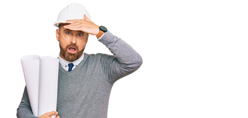 Handsome middle age man holding paper blueprints stressed and frustrated with hand on head,...