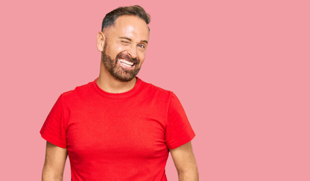 Handsome middle age man wearing casual red tshirt winking looking at the camera with sexy expression, cheerful and happy face.